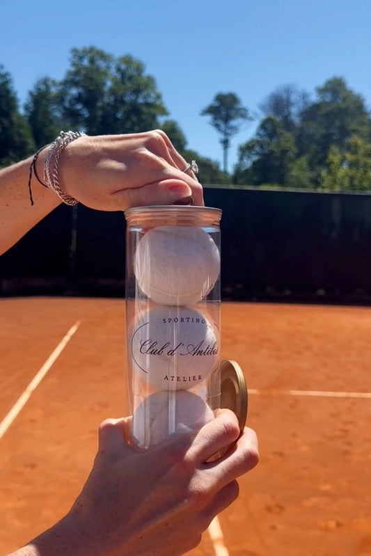 White Cd'A tennis balls on a red clay court