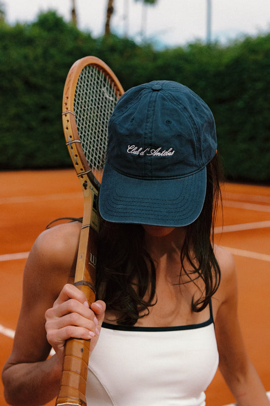 Woman wearing a navy cap with Club d'Antibes logo holding a vintage racquet