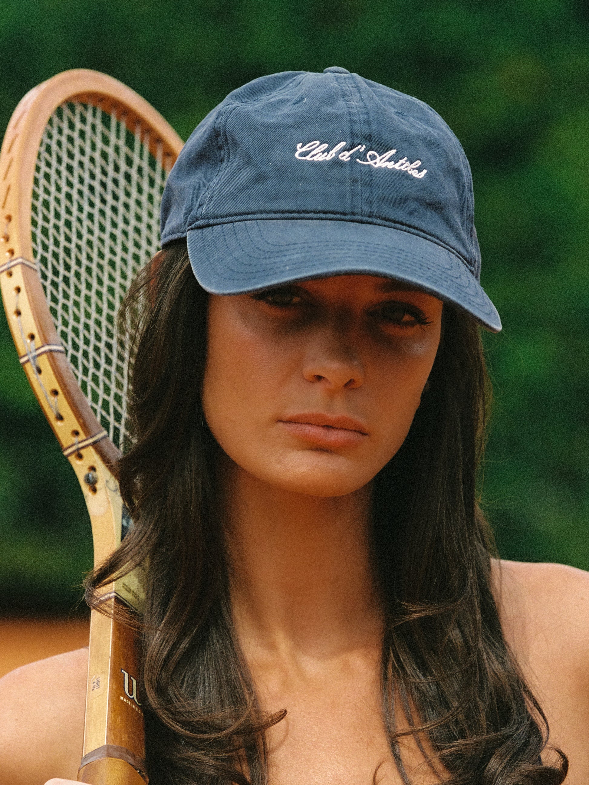 Woman wearing a navy cap with Club d'Antibes logo holding a vintage racquet