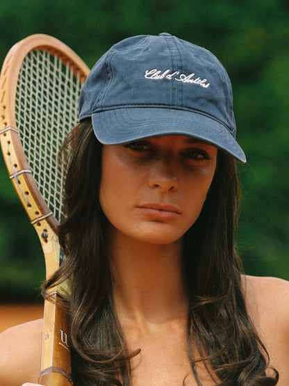 Woman wearing a navy cap with Club d'Antibes logo holding a vintage racquet